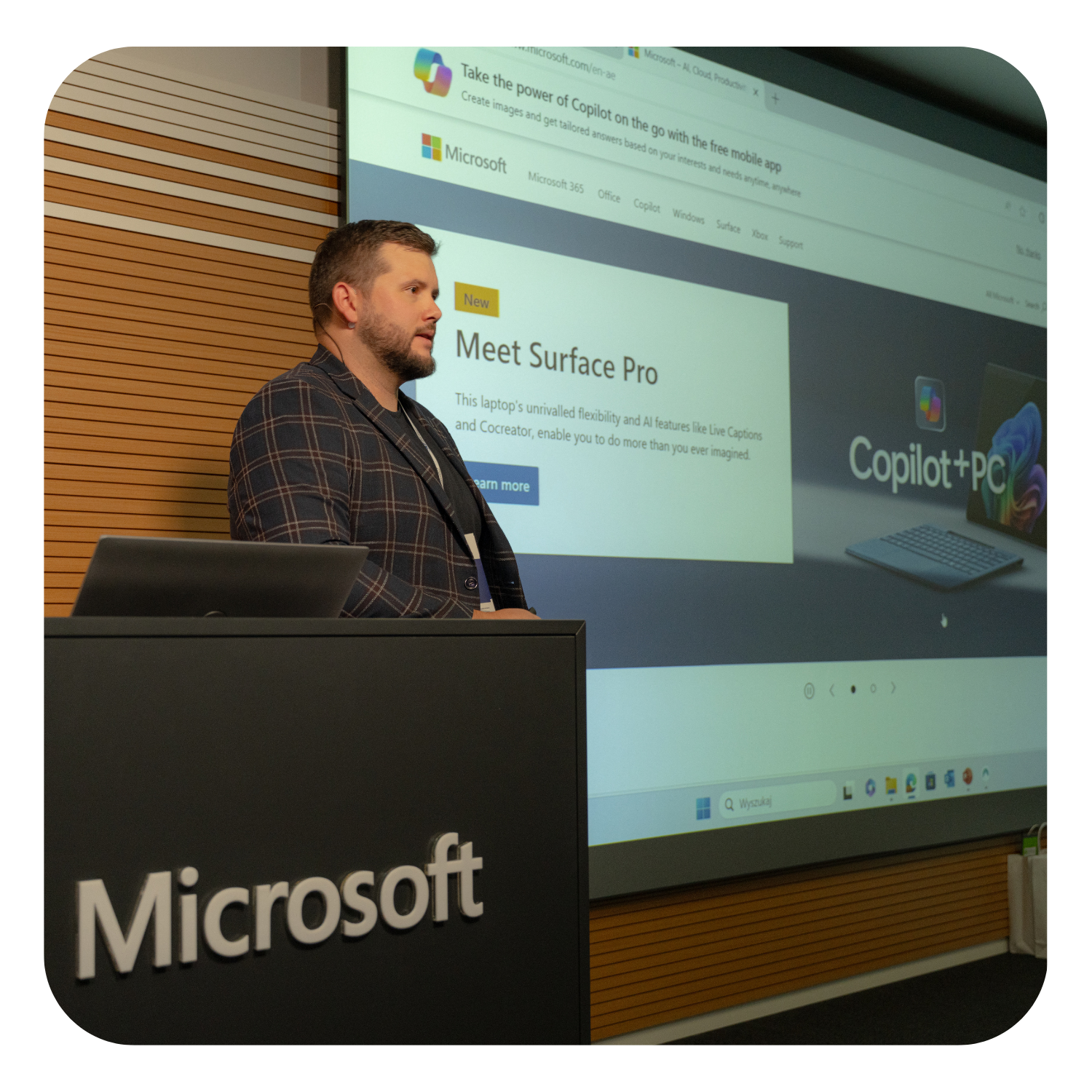 Presentation at Microsoft — speaker at the podium, showing Copilot+ PC / Surface Pro